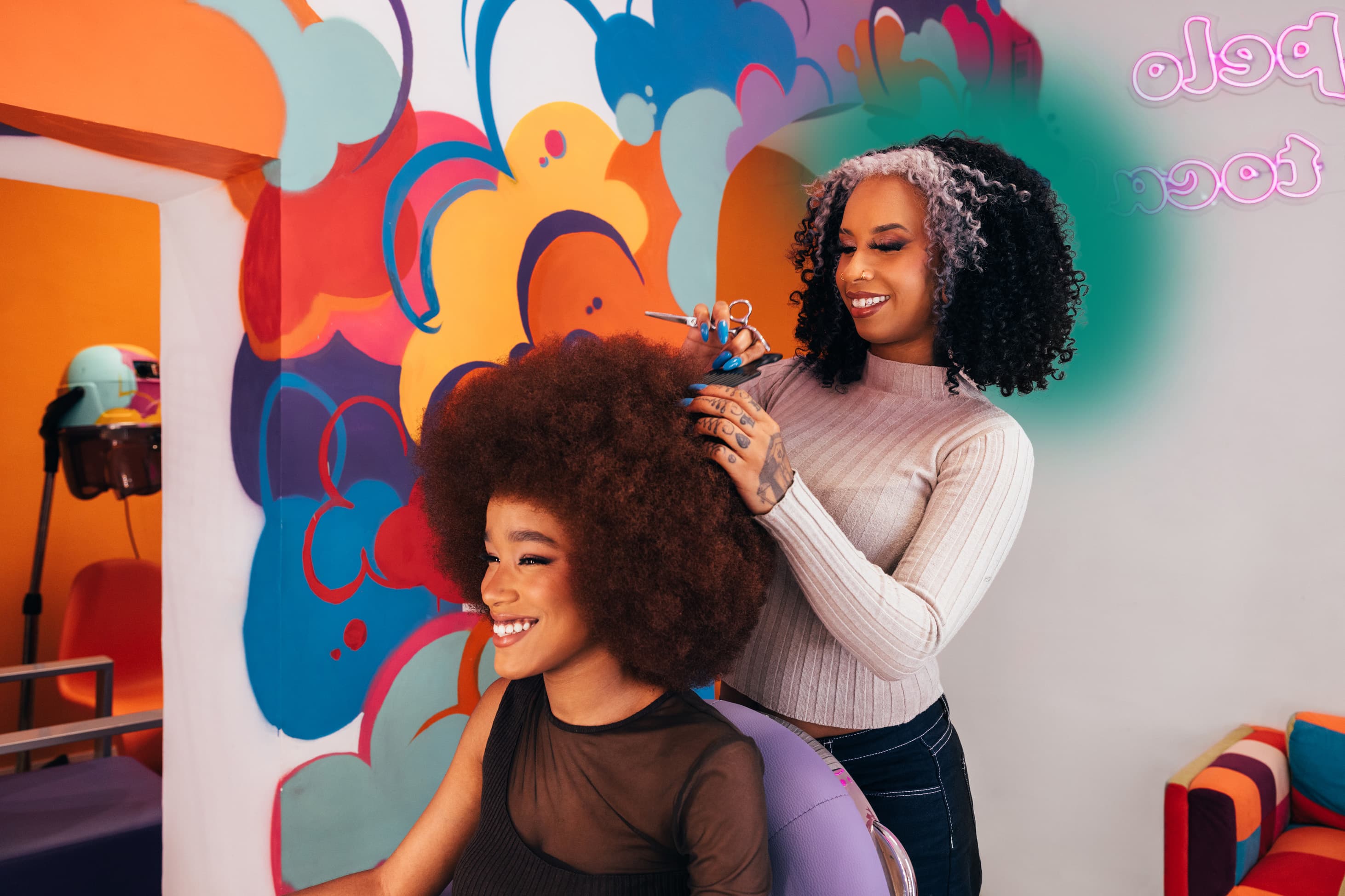 A stylist shaping a client's natural Afro in a colourful salon